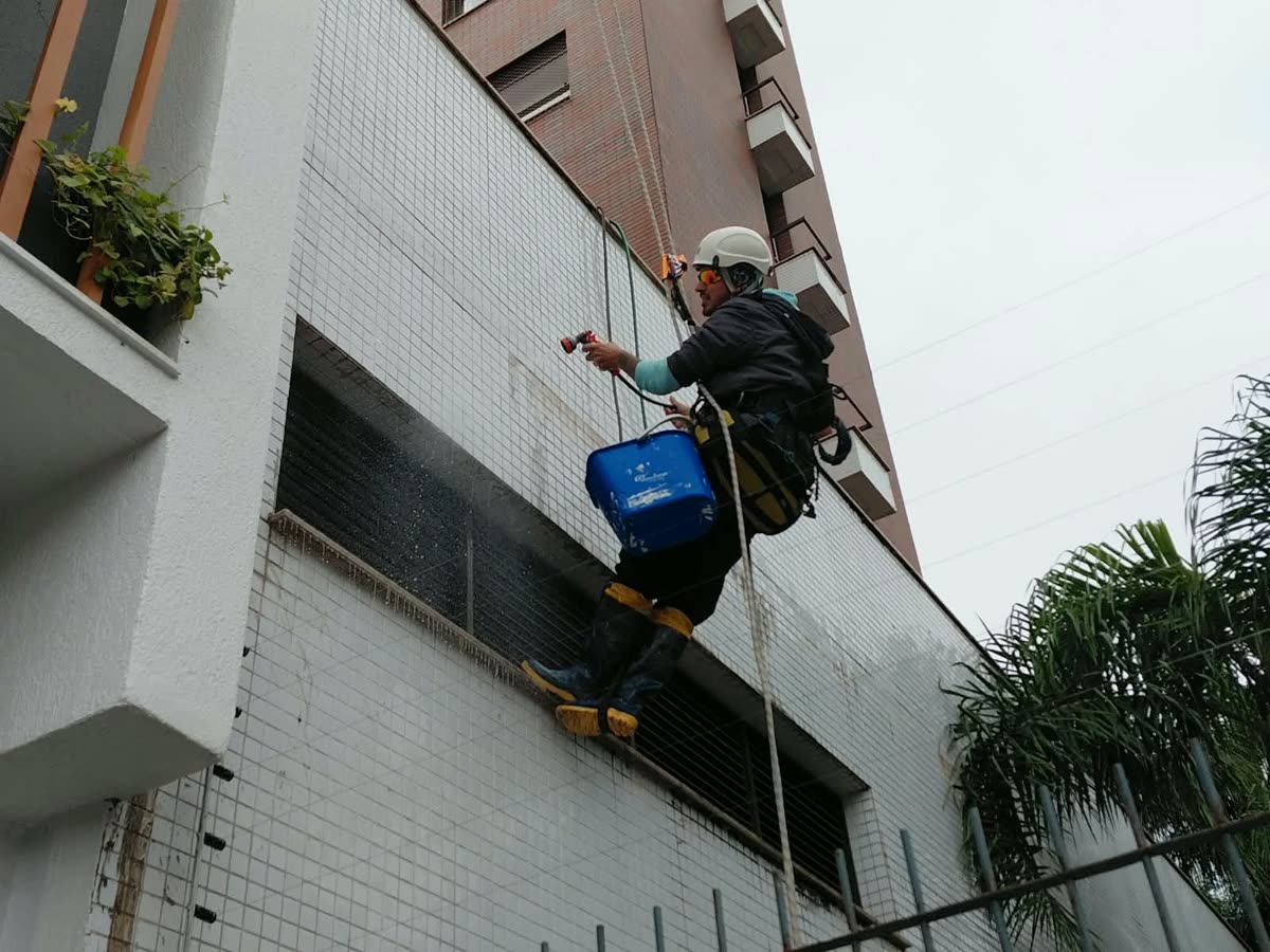 Técnico em acesso por cordas lavando fachada de pastilhas com jato de água