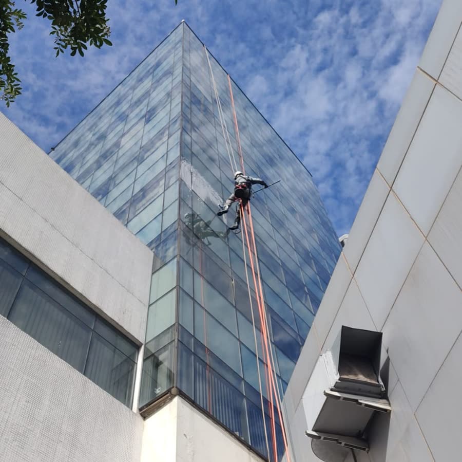Técnico em acesso por cordas limpando a pele de vidro de um prédio
